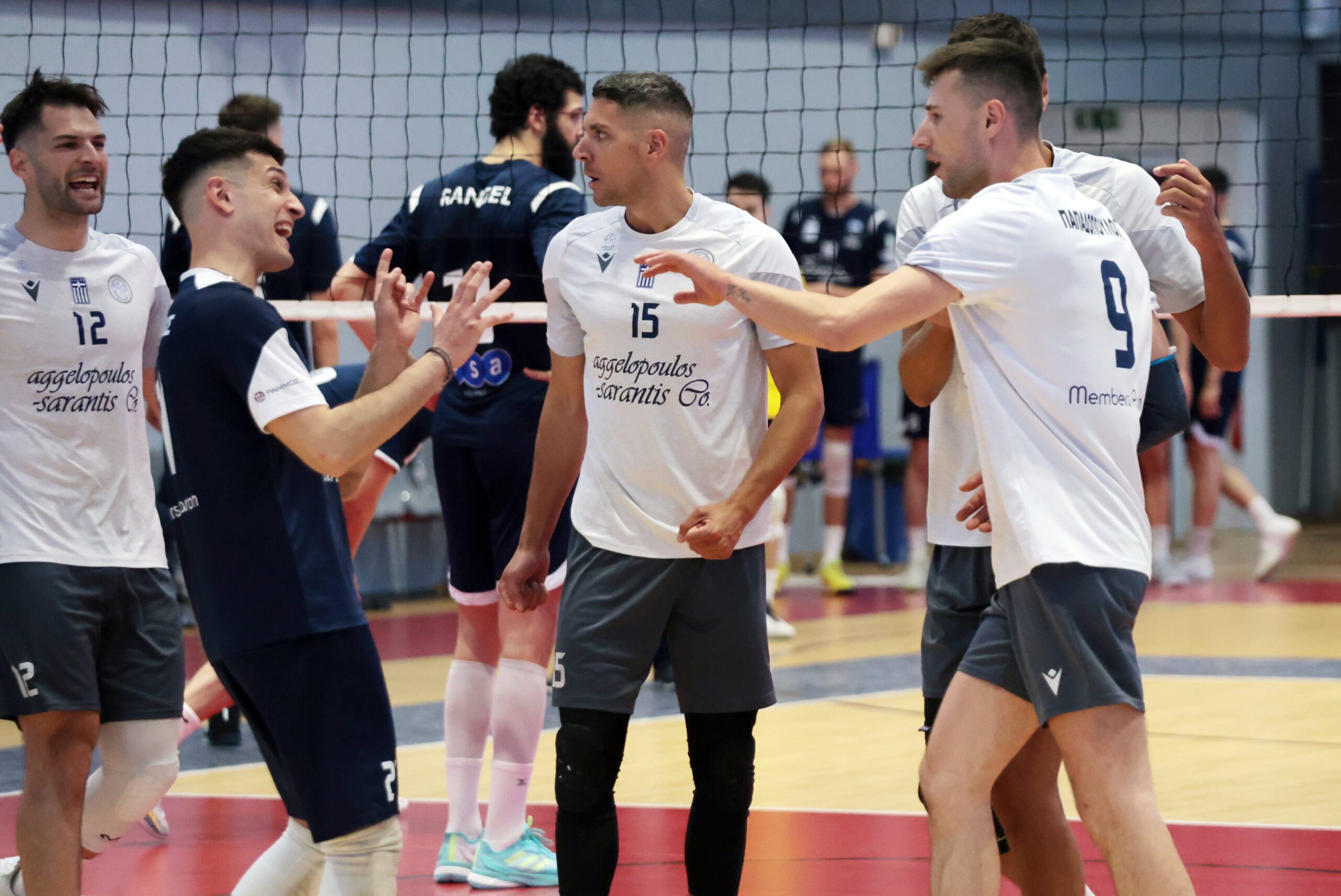 Group of volleyball players celebrate at the net, high fives and smiles in a gym setting.