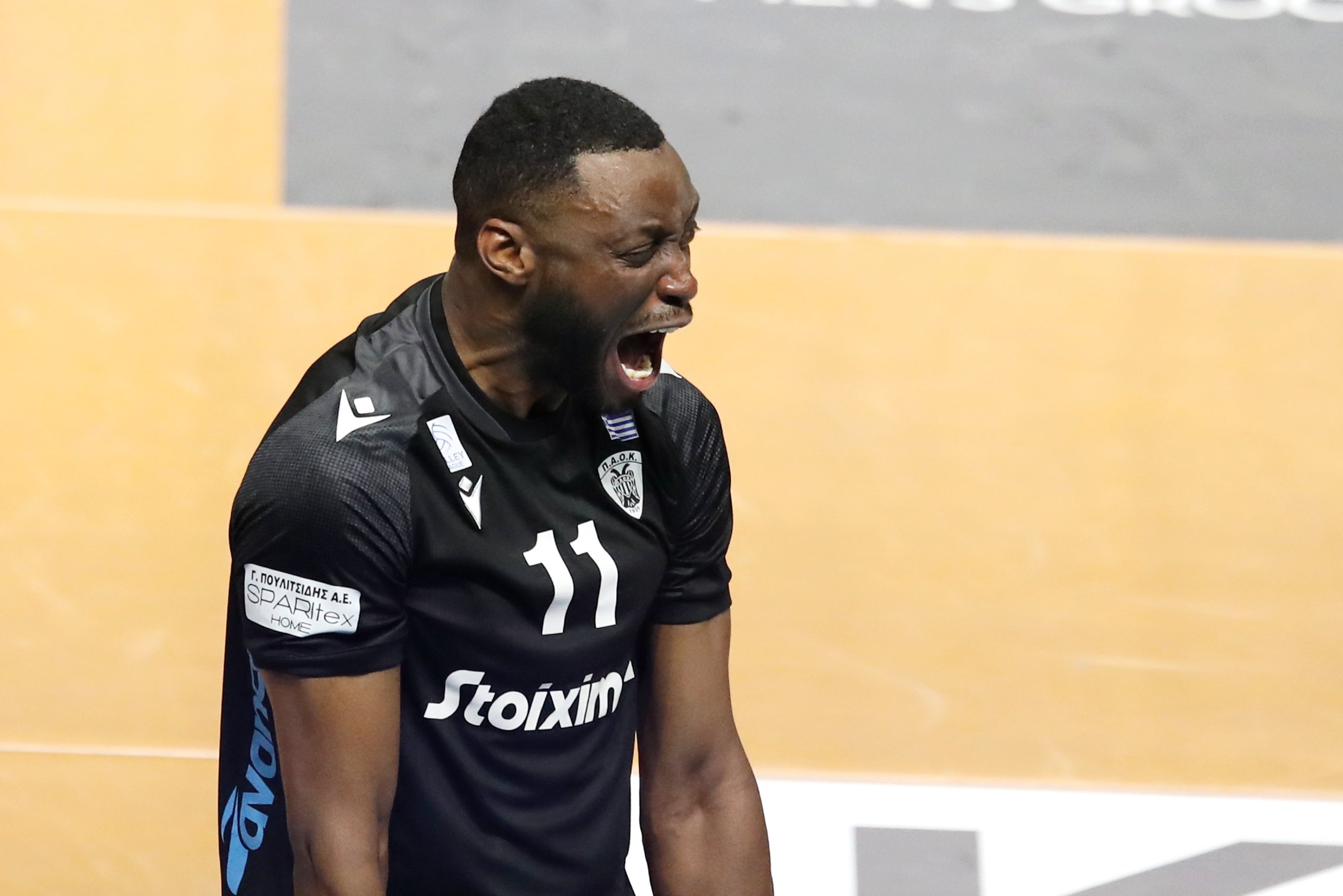 Athletic man in a black jersey with number 11 shouting with mouth open on an indoor court.