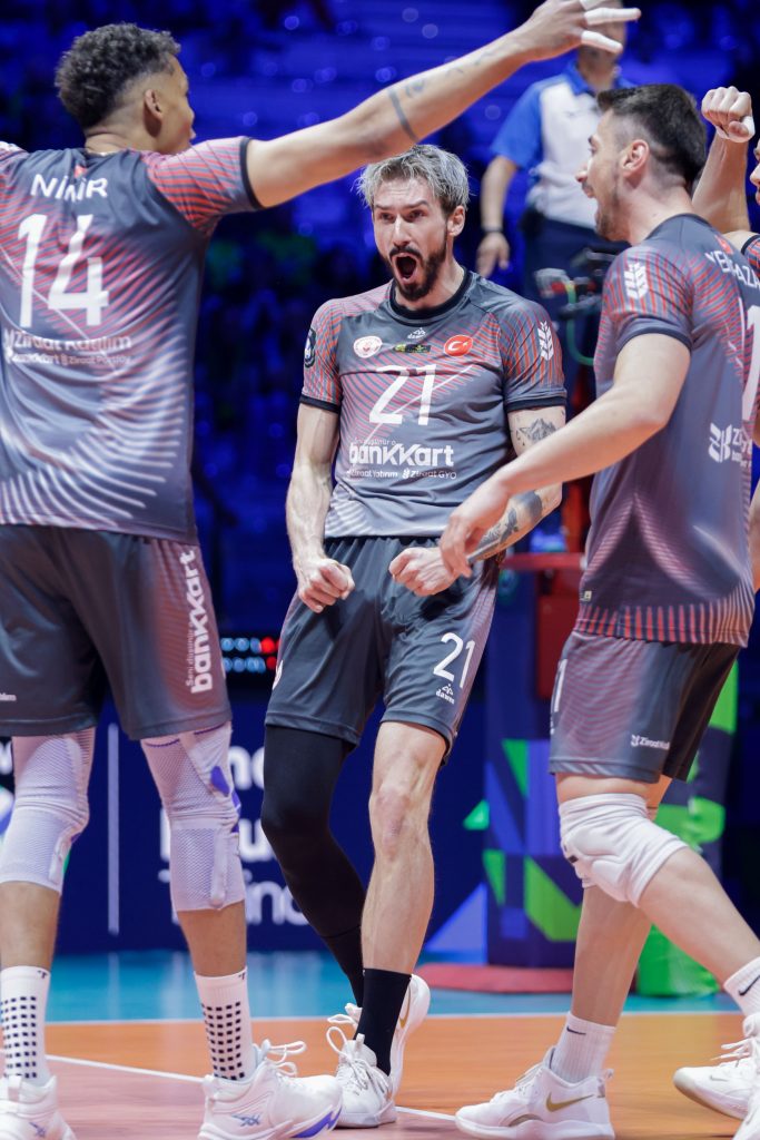 001 The Volley Lovers Volleyball players in gray uniforms celebrate on a court, arms raised in a cheer together.