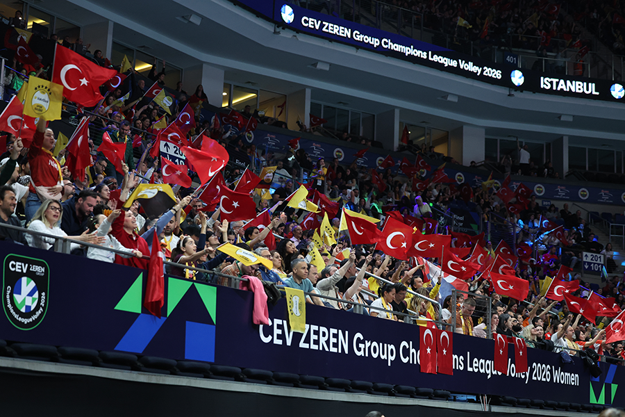 Crowd of spectators in a stadium, waving Turkish flags during a volleyball match with banners showing CEV ZEREN Group Champions League Volley 2026.
