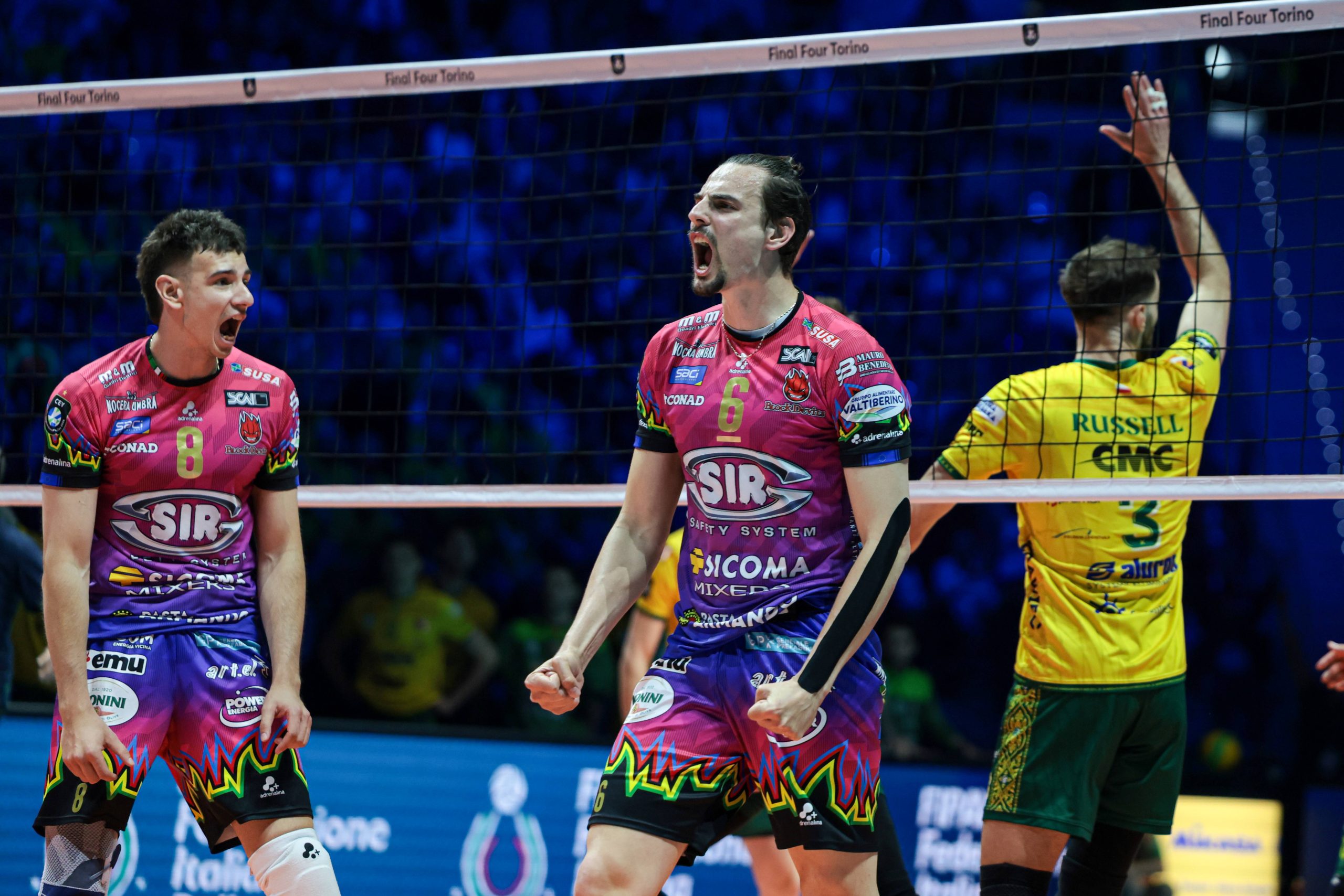 002 The Volley Lovers Three male volleyball players celebrate a point on an indoor court behind the net, two in pink uniforms and one in yellow.