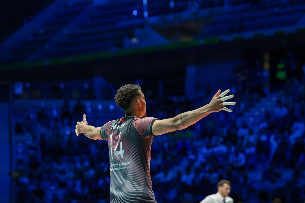 007 The Volley Lovers Athlete wearing a gray jersey with number 14, arms outstretched in a blue-lit arena with a cheering crowd in the background.