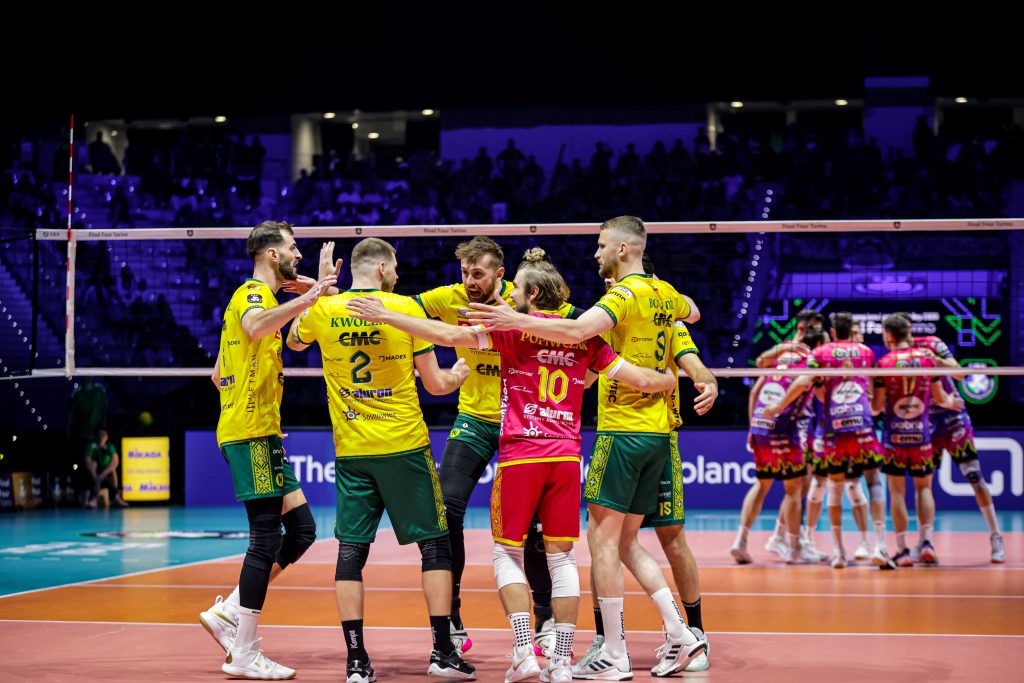 008 The Volley Lovers Volleyball players in yellow uniforms celebrate together at the net on an indoor court as fans watch from stands.