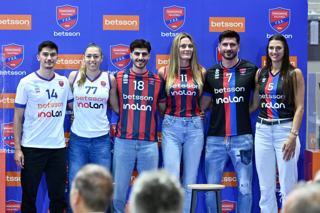 03 The Volley Lovers Six volleyball players pose for a group photo in front of a blue backdrop covered with sponsor logos.
