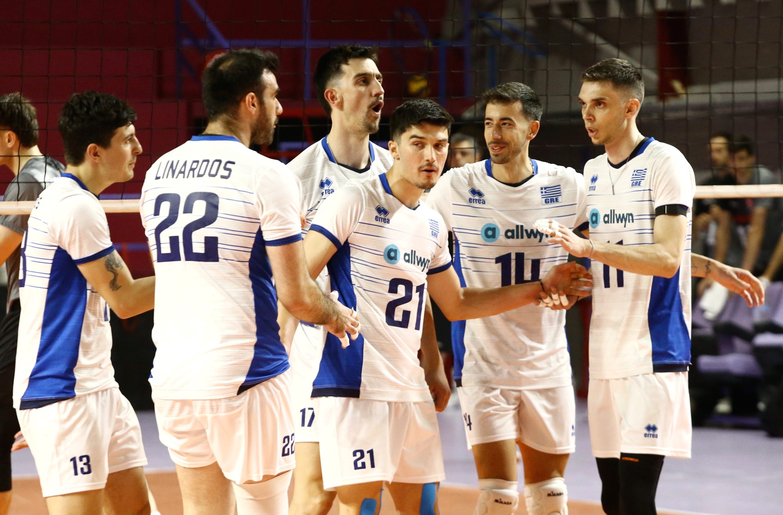 ÅËËÁÄÁ ÅËÂÅÔÉÁ<br>ÖÉËÉÊÏ The Volley Lovers Group of male volleyball players in white and blue uniforms huddling on an indoor court near the net.