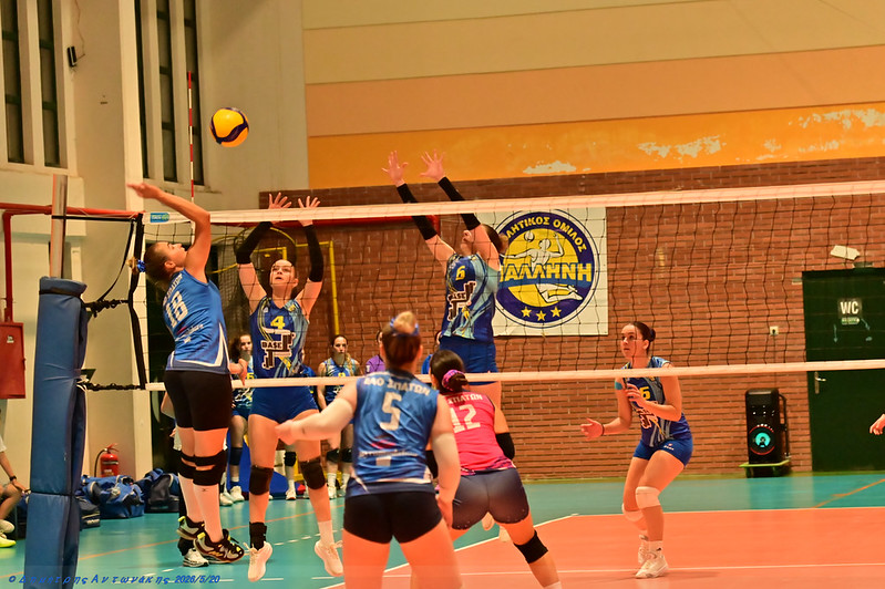 5528347143128d217903dc The Volley Lovers Indoor volleyball match: players in blue and pink uniforms contest at the net with a ball in the air.