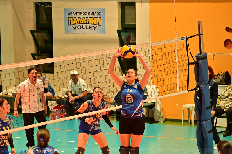 552834737865dc4afdb1dc The Volley Lovers Blue team player (#11) lifts the ball for a set at the net as teammates and a referee watch in a gym volleyball match.