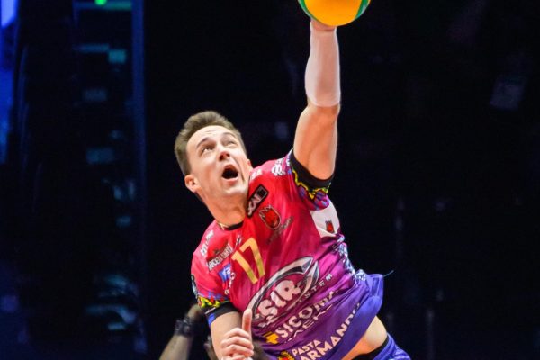 Male volleyball player in a colorful uniform jumps to spike a yellow ball over the net.