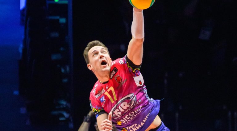 Male volleyball player in a colorful uniform jumps to spike a yellow ball over the net.
