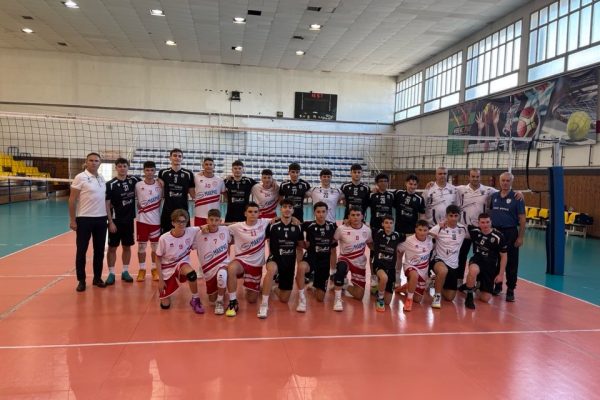 Group of volleyball players and coaches pose on an indoor court after a match, wearing white, red, and black uniforms.