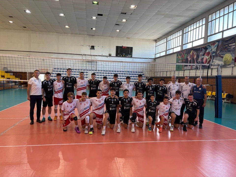 Group of volleyball players and coaches pose on an indoor court after a match, wearing white, red, and black uniforms.
