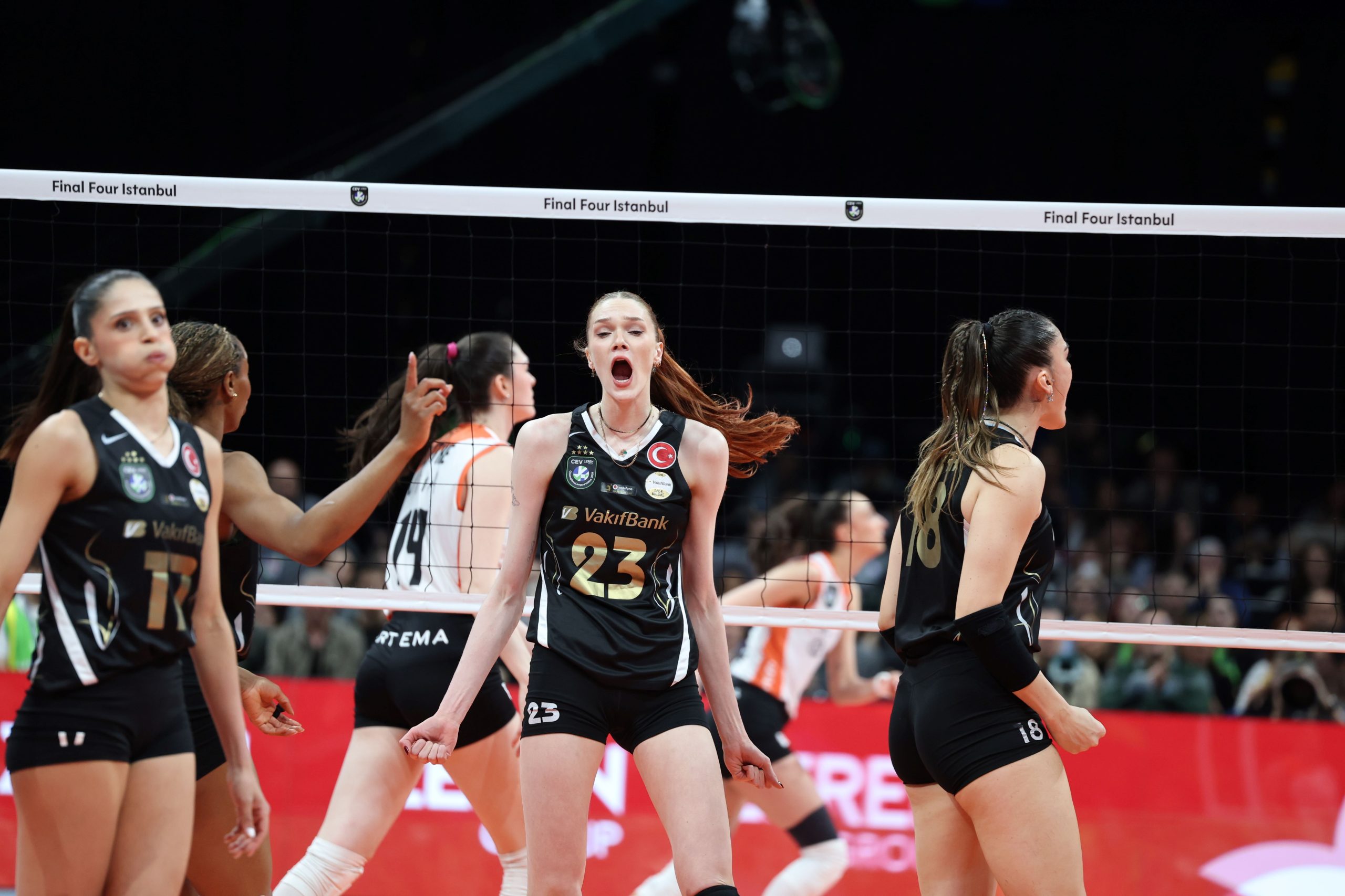 IMG6061 The Volley Lovers Female volleyball players in black uniforms celebrate near the net during a match in an arena, central player shouting with fist raised (jersey 23).