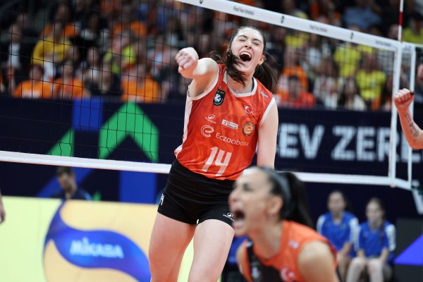 Volleyball player in orange jersey (#14) celebrates a point at the net with cheering crowd in background.