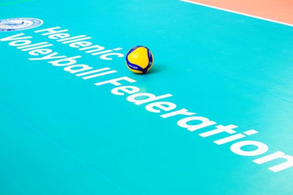 Volleyball resting on a bright turquoise court with the words 'Hellenic Volleyball Federation' and a logo in the corner.