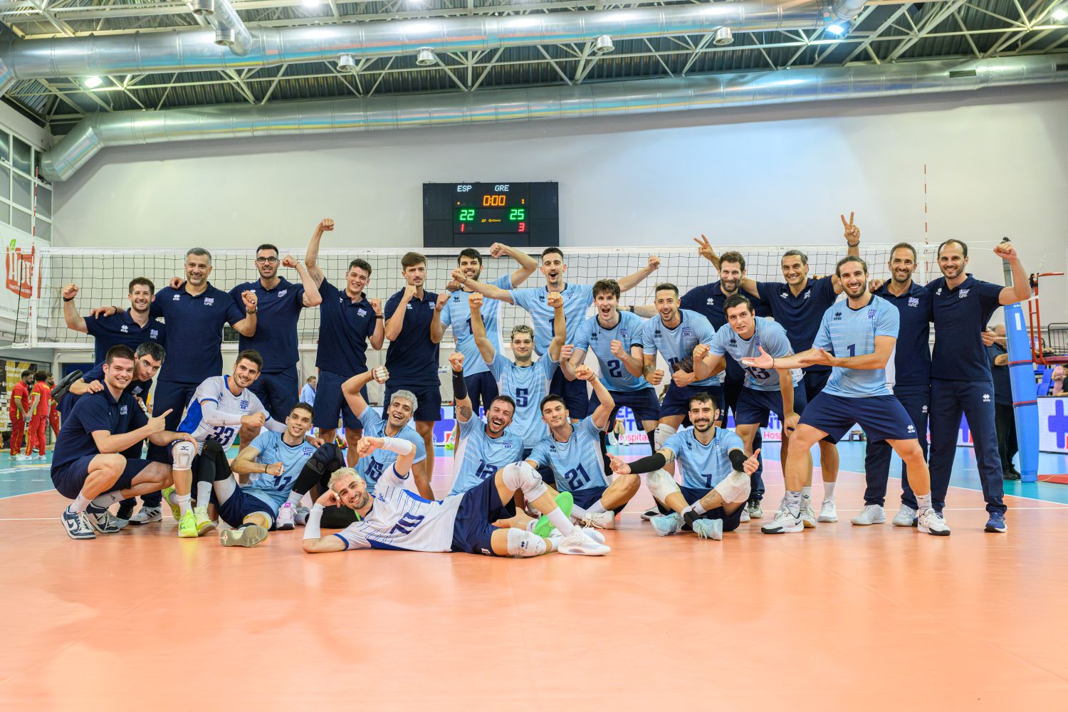 mennt The Volley Lovers Volleyball team celebration on the court: players and coaches pose with raised fists in front of the net in a gymnasium behind them.