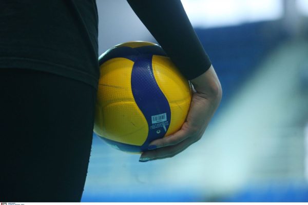 Close-up of a hand gripping a yellow and blue volleyball held by a person in a dark outfit.