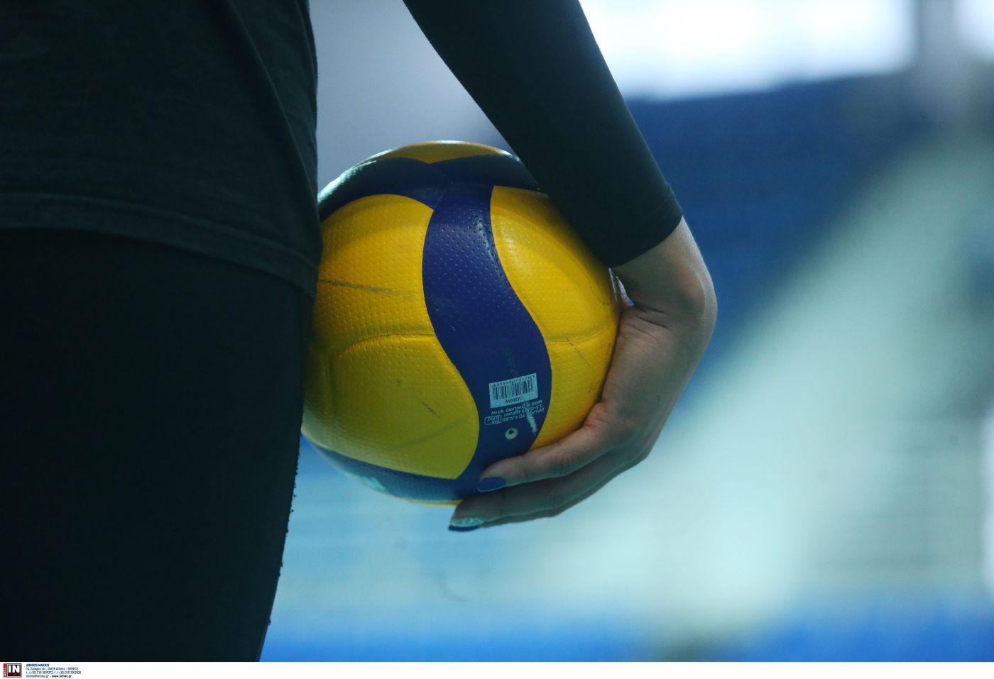 Close-up of a hand gripping a yellow and blue volleyball held by a person in a dark outfit.