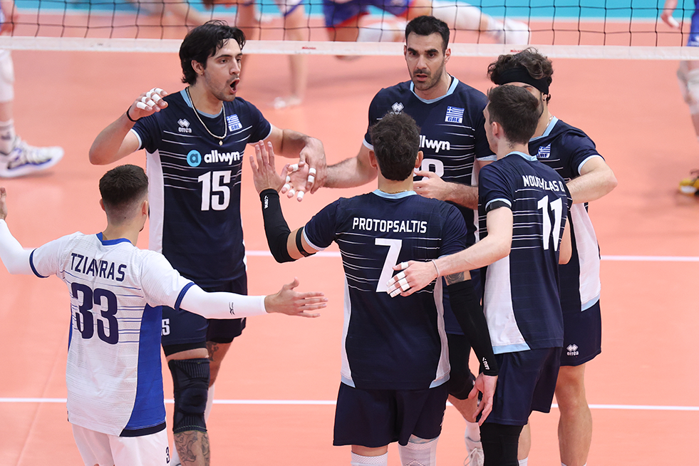 000 The Volley Lovers Group of Greek volleyball players in navy jerseys celebrate with high-fives on an indoor orange court.