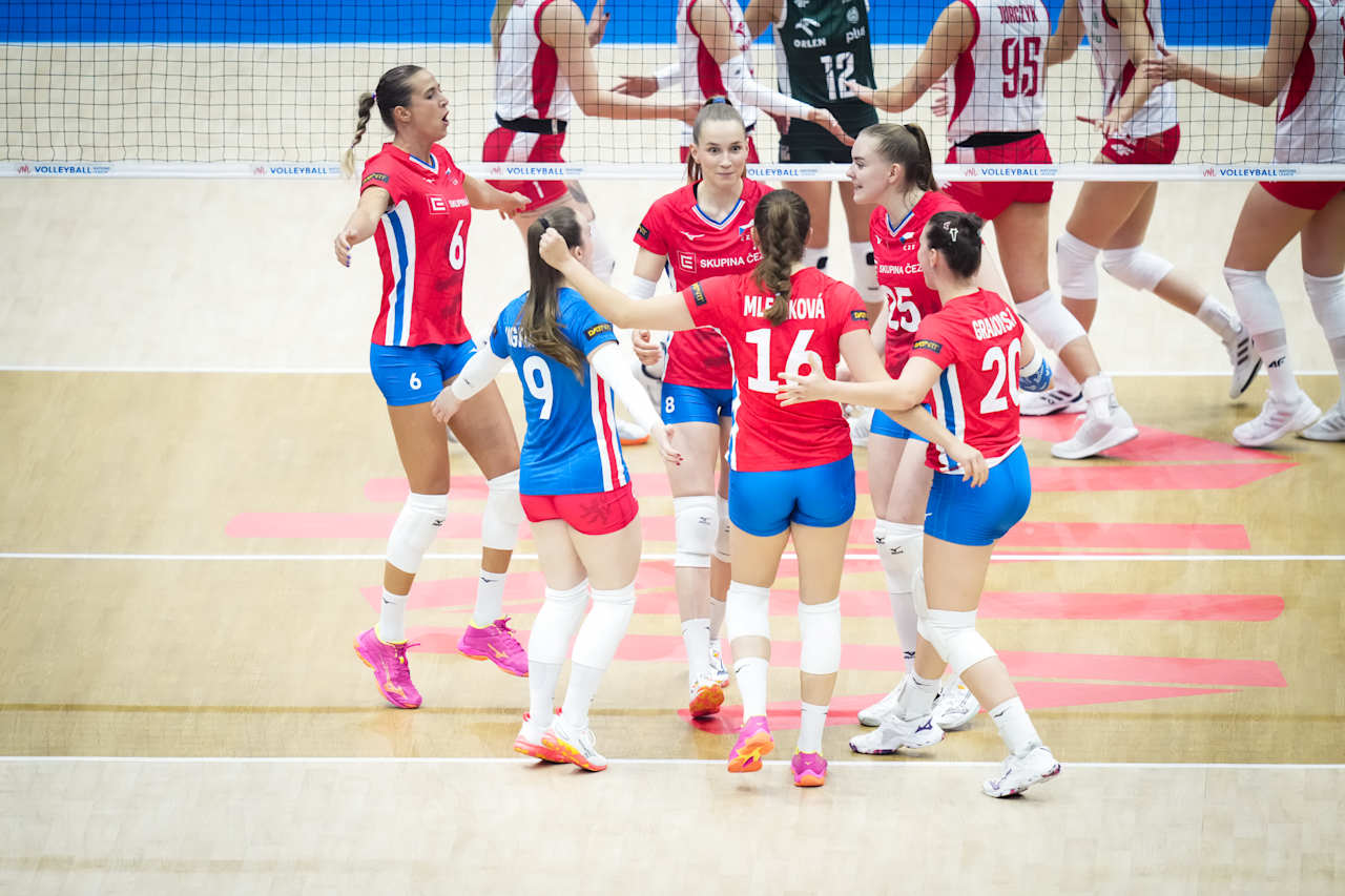 02 The Volley Lovers Group of volleyball players in red and blue uniforms celebrate together on a bright indoor court near the net, pink shoes visible.
