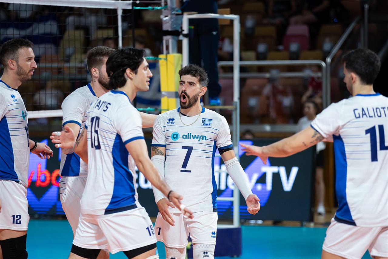 Greek men's volleyball team celebrates on the court, high-fiving and shouting after a point near the net.