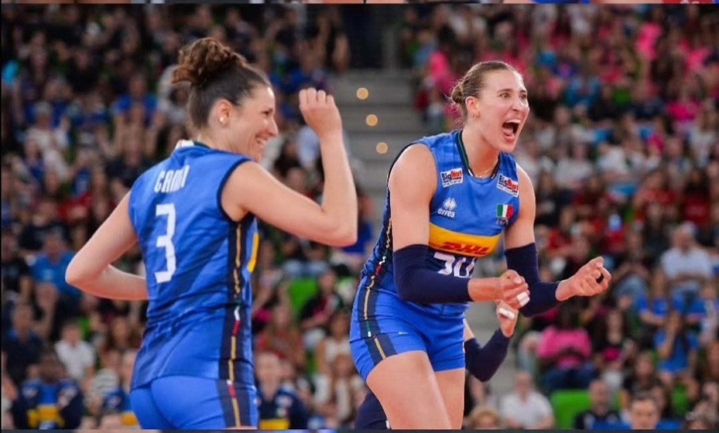 7041496061222236035003122902780655326902268351n The Volley Lovers Two female volleyball players in blue uniforms celebrate a point on the court as the crowd cheers in the stands.