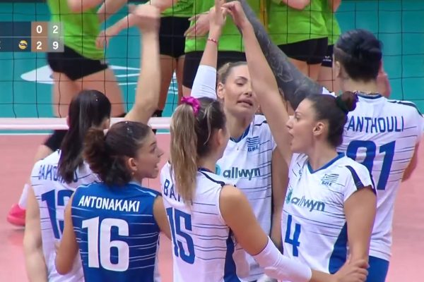 Volleyball teammates in blue and white uniforms celebrate a point with a group hug on the court.