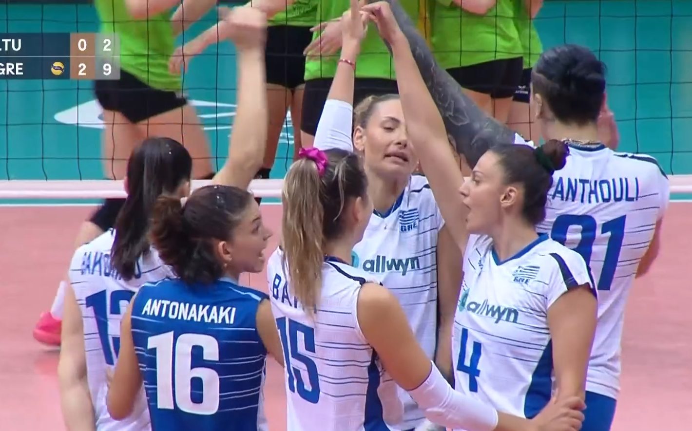 Volleyball teammates in blue and white uniforms celebrate a point with a group hug on the court.