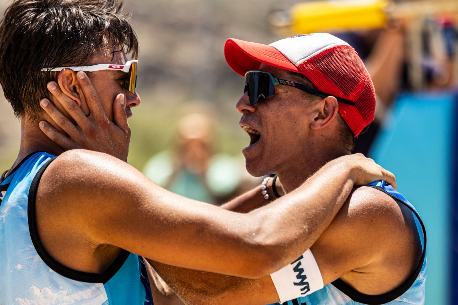 ntallaschatz324 The Volley Lovers Two athletes in blue uniforms embrace, one with a red cap shouting or cheering in celebrationor encouragement, outdoor setting with blurred background.
