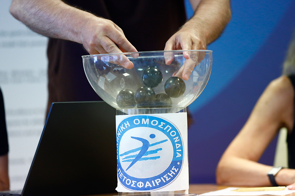 5266962000 The Volley Lovers Hands reach into a glass bowl of dark balls for a raffle on a pedestal with a blue Greek federation emblem nearby.