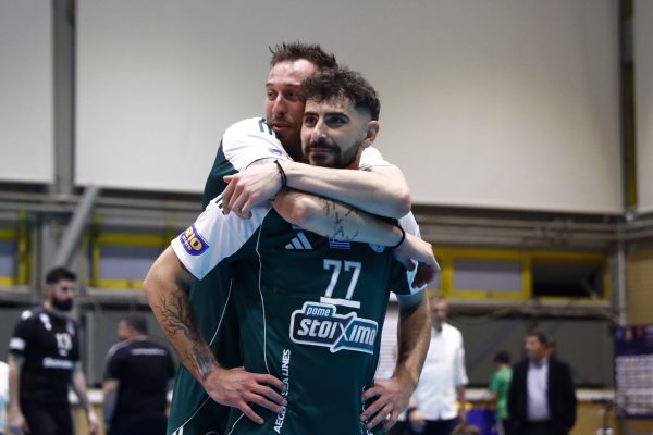 Two male teammates in green uniforms share a hug in an indoor sports venue, cheering after a game.