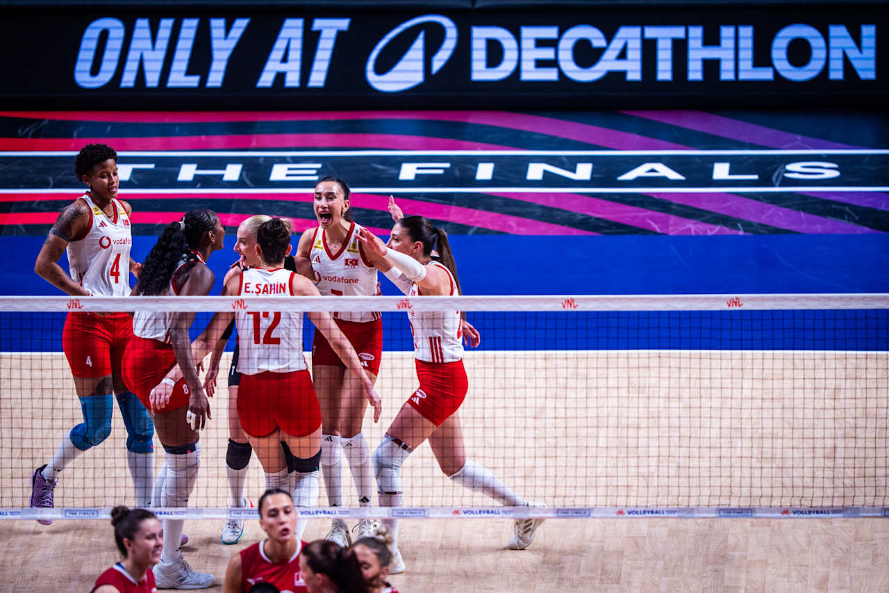 Women’s volleyball team celebrates together on court during the finals, banners reading “THE FINALS” behind them.