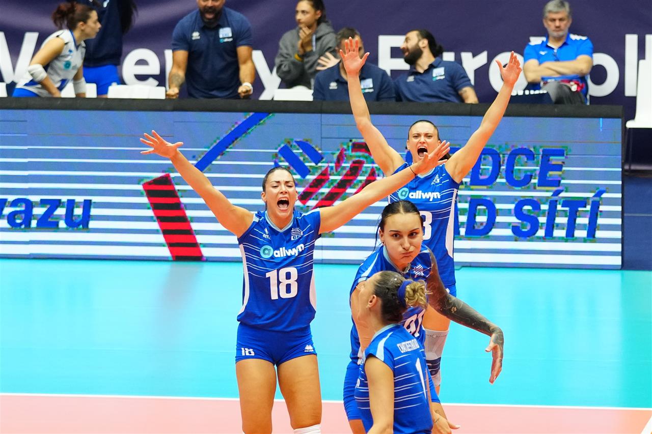 164929FRA GRE 30082026 24 The Volley Lovers Women’s volleyball team in blue uniforms celebrates on the court with arms raised in victory.