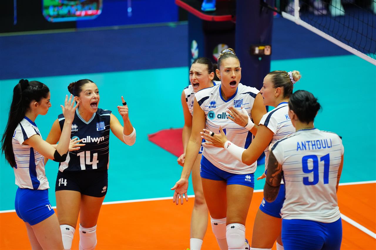 212822příjezd CZE GRE cev 21082026 24 The Volley Lovers A group of female volleyball players wearing white and blue celebrate on an indoor court after a point, with arms raised in excitement.