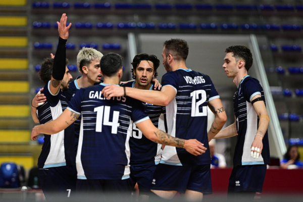 Team of male volleyball players in navy uniforms huddles together on an indoor court, number 14 and 12 visible on jerseys.