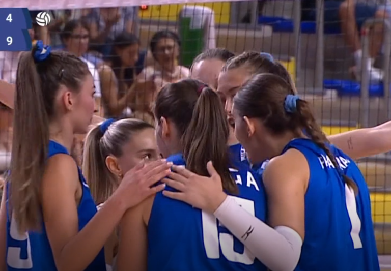 image The Volley Lovers Female volleyball players in blue uniforms huddle with arms around each other on the court during a match, scoreboard visible in the corner showing 4-9