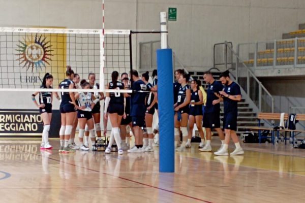 Volleyball team in blue uniforms huddling near the net on an indoor court.