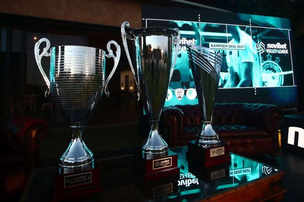 Three large silver trophies on a glass table during a sports awards event, with a digital screen backdrop displaying league branding.
