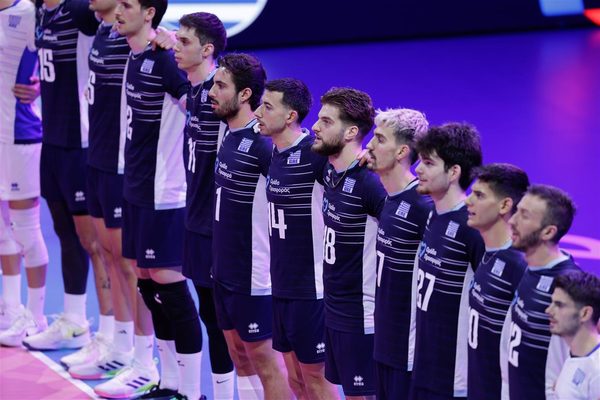Men's volleyball team lined up together with arms around each other before a match on a purple-lit court, wearing navy uniforms.