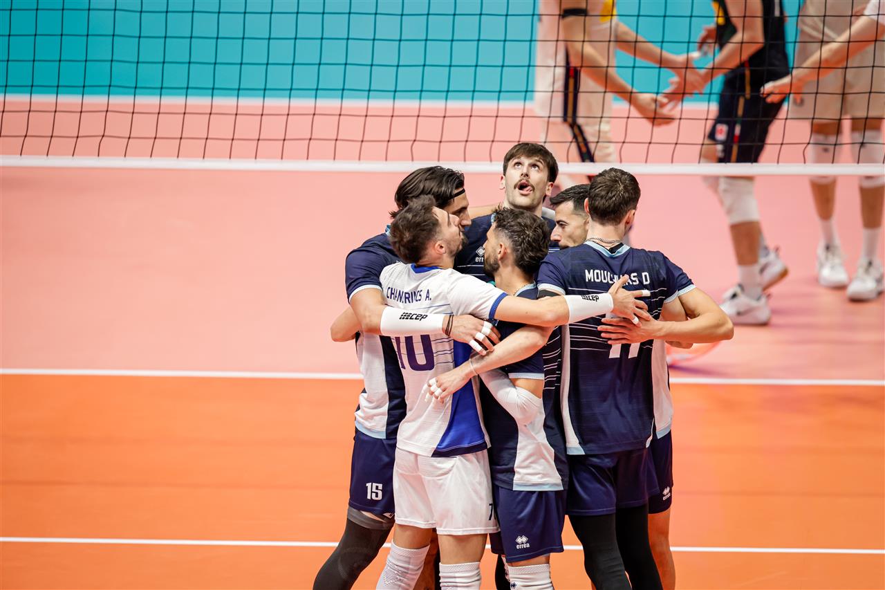 222446I8A2725 The Volley Lovers A group of male volleyball players in navy and white uniforms hug in celebration on an orange indoor court near the net.