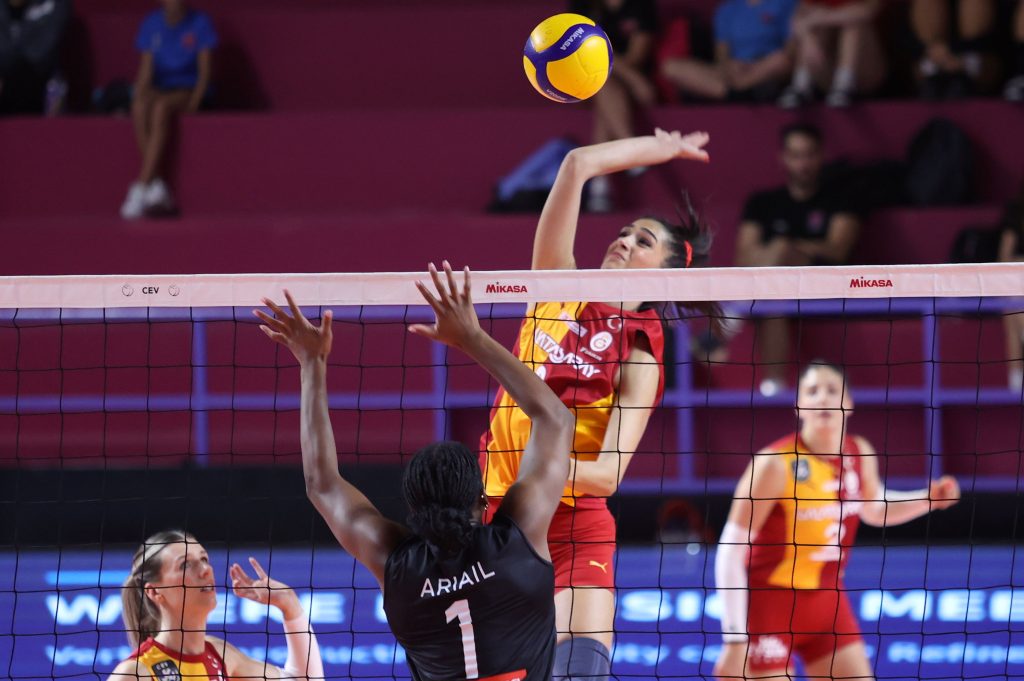 5356447 The Volley Lovers Women’s volleyball game: a player in red and yellow spikes at the net while an opponent in black blocks. The yellow ball hovers above the net.