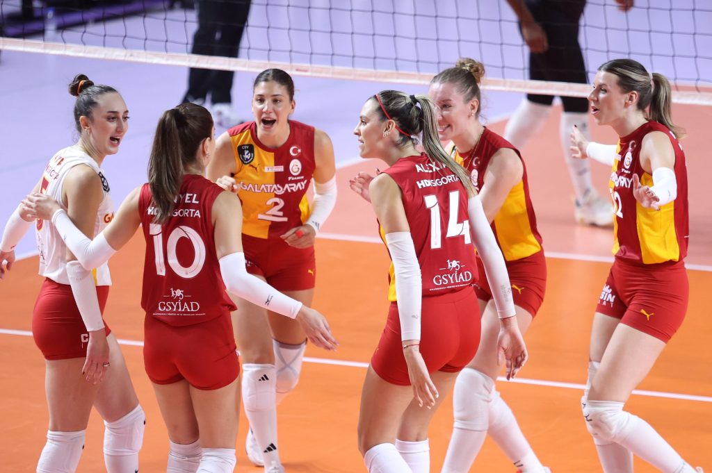 5356507 The Volley Lovers Group of female volleyball players in red uniforms celebrate together on an indoor court, forming a huddle near the net.