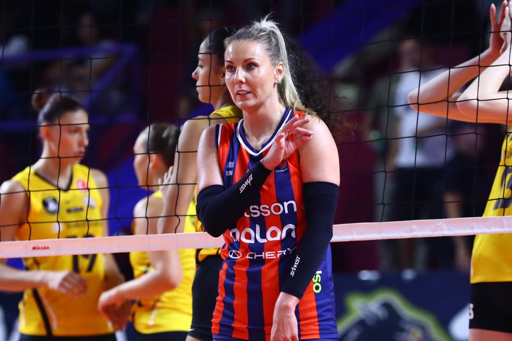 Intime Sarelas Dimitris The Volley Lovers Female volleyball player in a red-and-blue striped uniform near the net, gesturing with her right hand while facing the court.