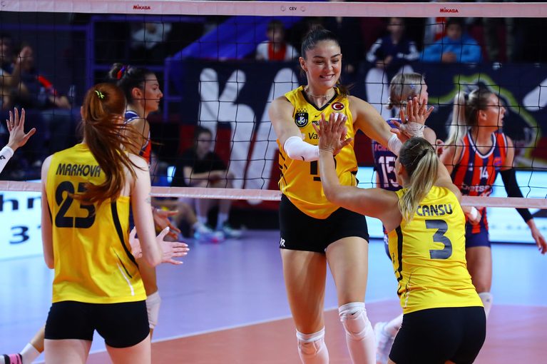 Volleyball players in yellow jerseys celebrate with high fives near the net during a match.