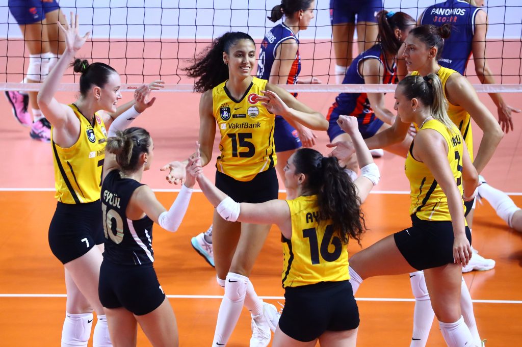 5357018 The Volley Lovers Women volleyball players in yellow uniforms high-fiving each other near the net on an orange court during a match.