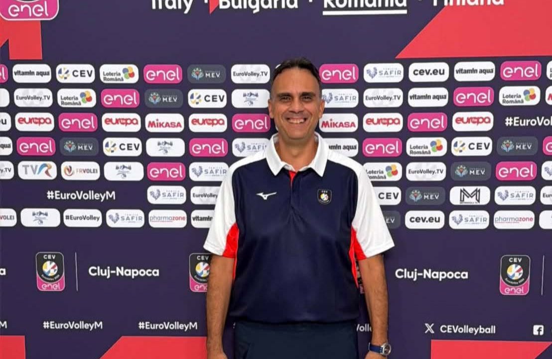 80158574715538547301190777887299686648976480n The Volley Lovers Man posing in front of a CEV EuroVolley 2026 backdrop, wearing a navy polo with white sleeves and dark pants.