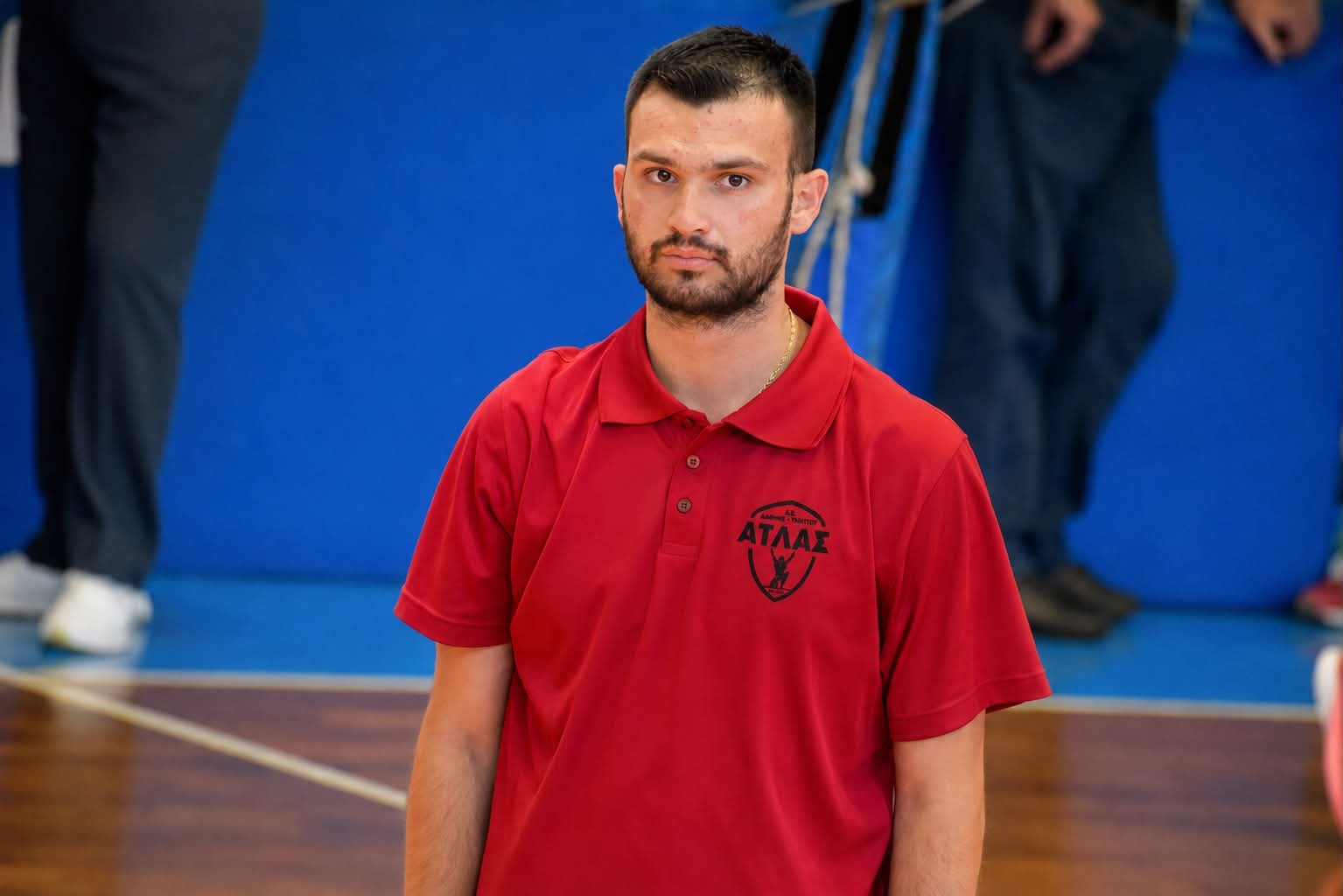 80474b9bc658421aada79f7e44cccc50 The Volley Lovers Young man in a red polo shirt with a logo stands in a gym with a blue padded wall behind him, looking at the camera.