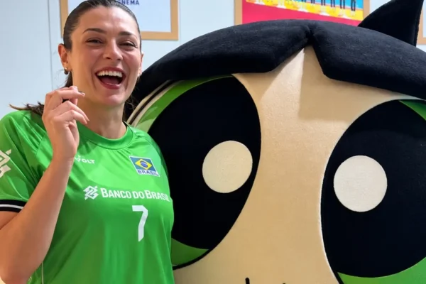 Smiling woman in a green Brazil soccer jersey (number 7) posing next to a large cartoon mascot.
