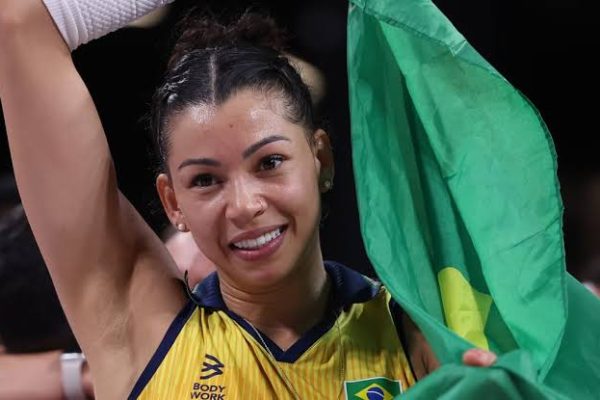 Smiling Brazilian female athlete raising her arm in celebration with a green flag.