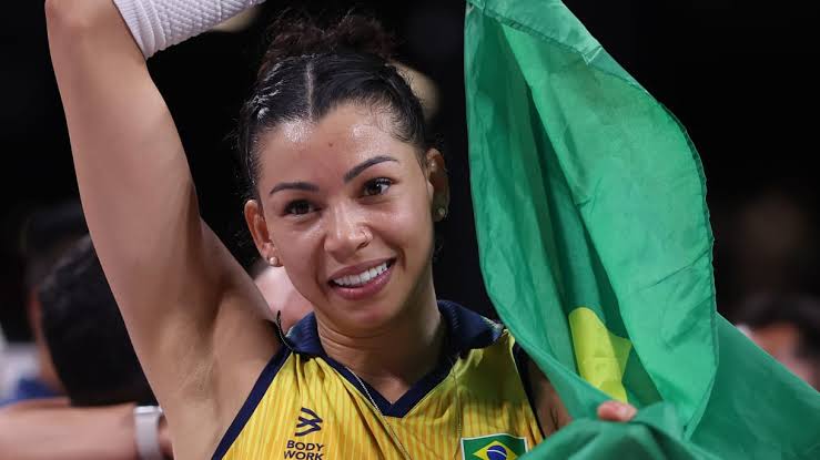 Smiling Brazilian female athlete raising her arm in celebration with a green flag.