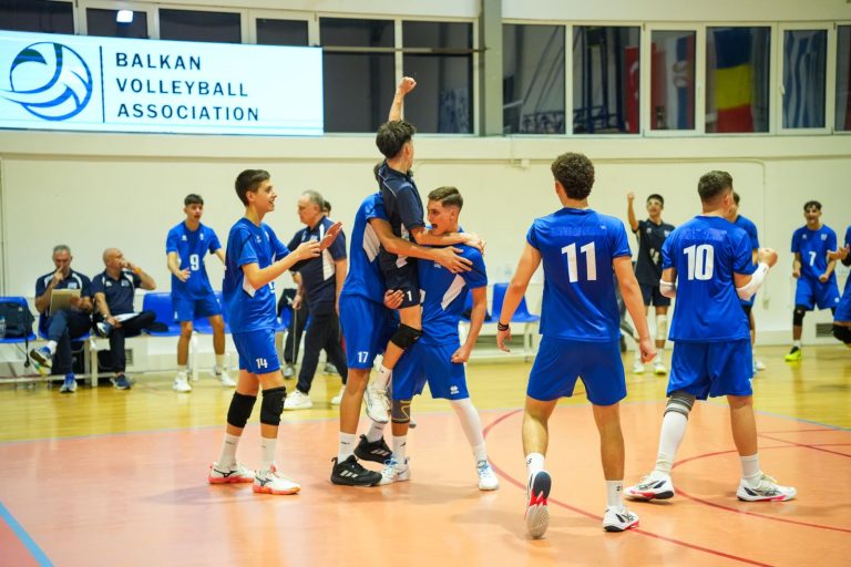 viberimage20260901224720067 The Volley Lovers Teenage volleyball players in blue uniforms celebrate on an indoor court, one lifting a teammate as others cheer; Balkan Volleyball Association banner visible in the background.